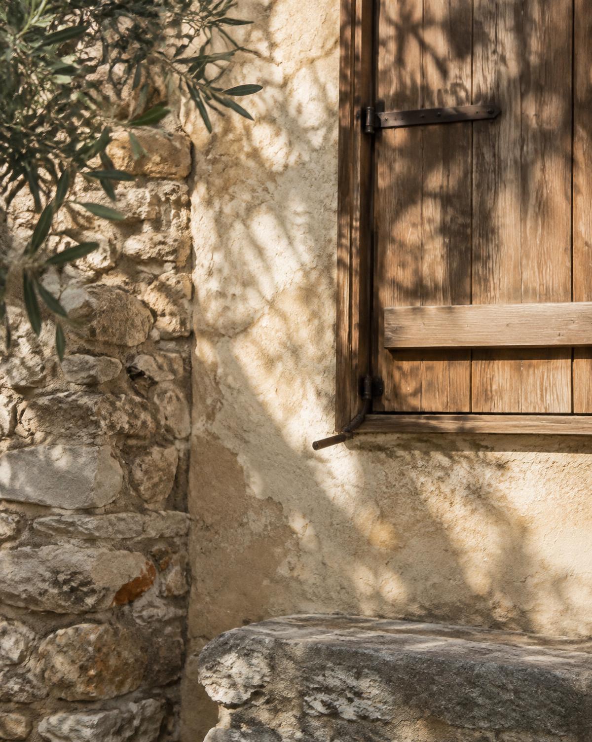 Local limestone wall, lime plaster and an aged oak shutter in afternoon sun